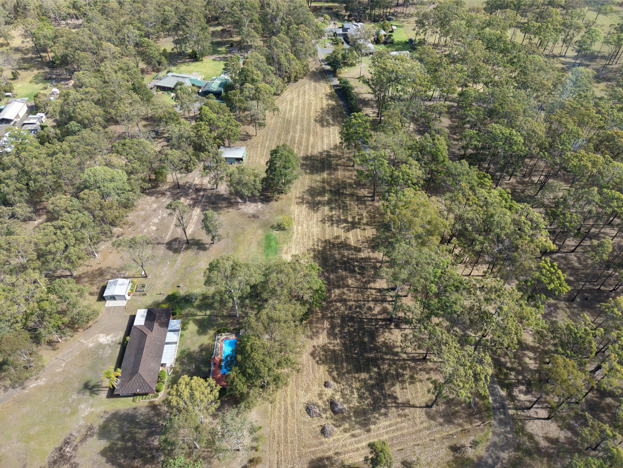Aerial view of service areas featuring lush trees, residential homes, and a swimming pool in a serene countryside setting.