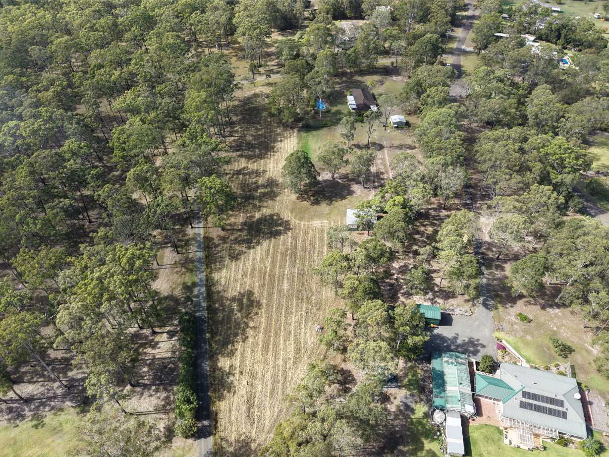 Service area aerial view featuring houses, dense trees, a dirt road, and a cleared field, showcasing the landscape.